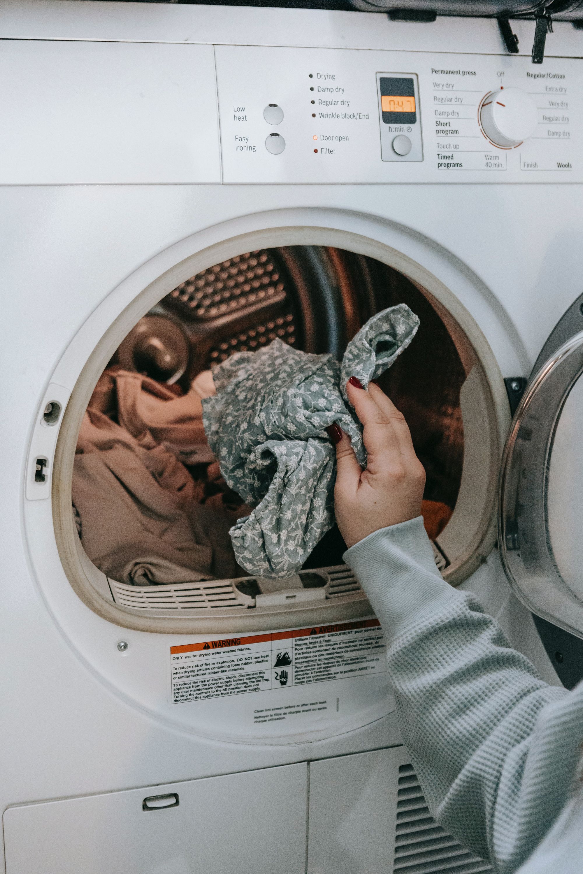 hand of a lady putting in floral clothes into a washing machine