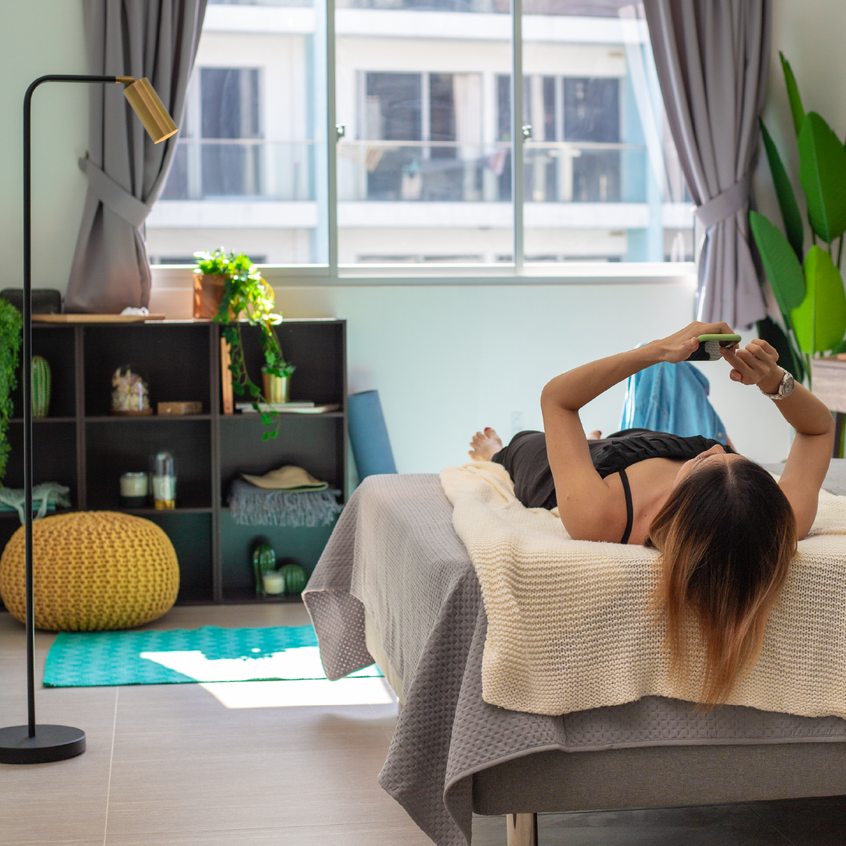 woman in her own room on bed lying down, scrolling her iphone