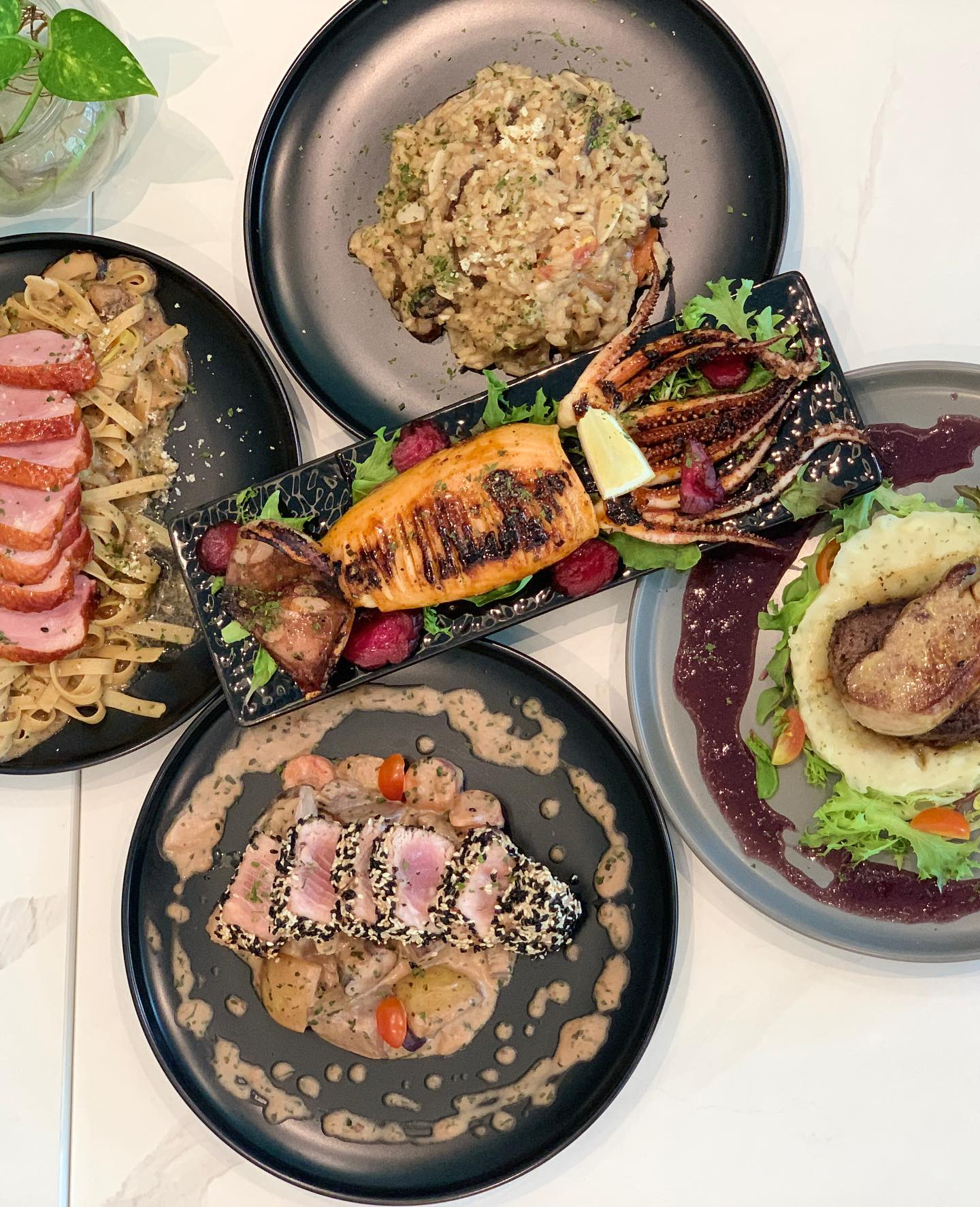 5 different menu served on the table. Giant squid in the middle, pasta, risotto and steak on the side