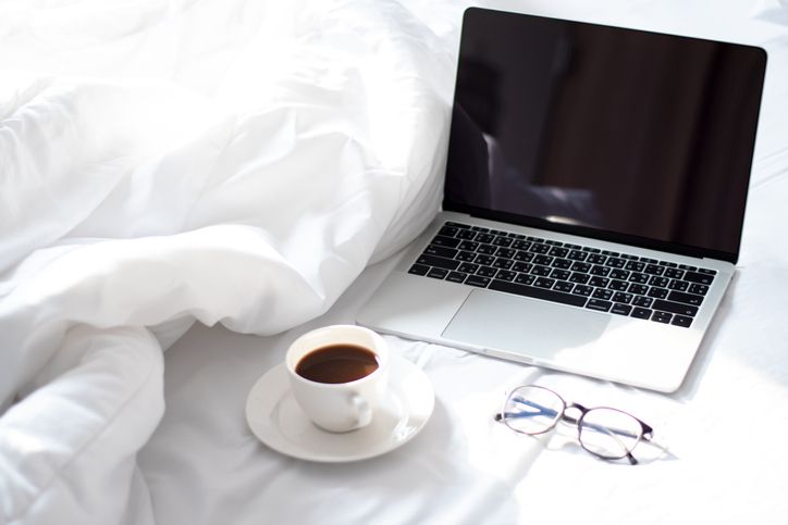 coffee mug, laptop and spectacles on a bed
