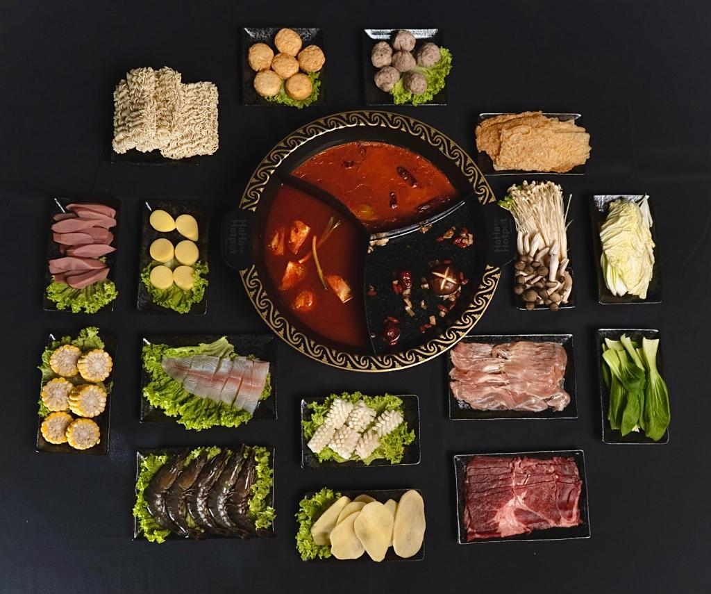 a hotpot bowl in the middle with many dishes such as vegetables, seafood and meat buffet