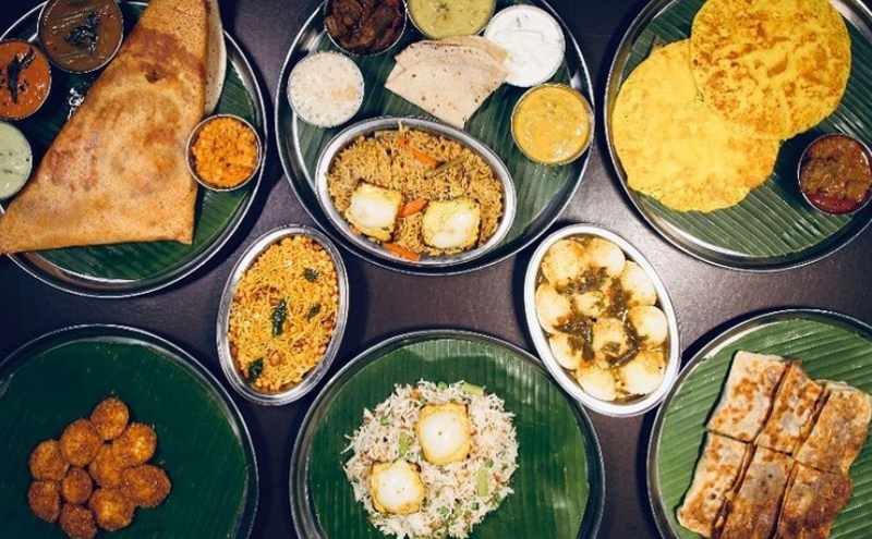 different types of vegetarian indian food such as dosai, capati served on a banana on top of a metal plate